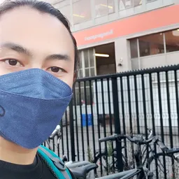 Persoon met blauw mondmasker voor winkelgevel met zwart hek
