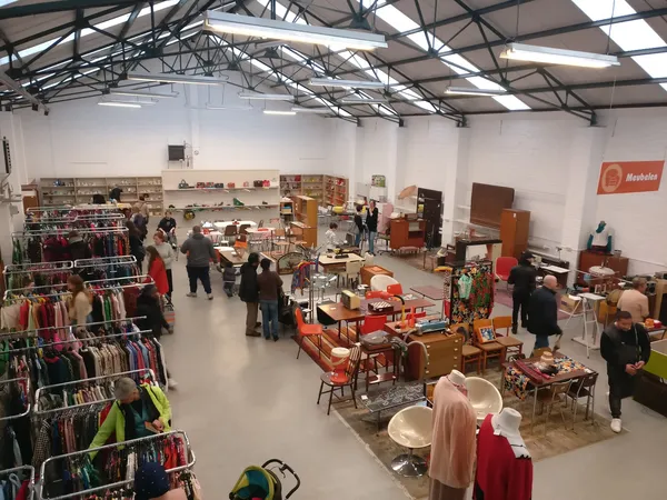 Overzicht van de winkelvloer met kleding aan rekken, meubels, huishoudartikelen en bezoekers die rondkijken