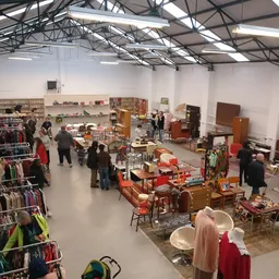Overzicht van de winkelvloer met kleding aan rekken, meubels, huishoudartikelen en bezoekers die rondkijken