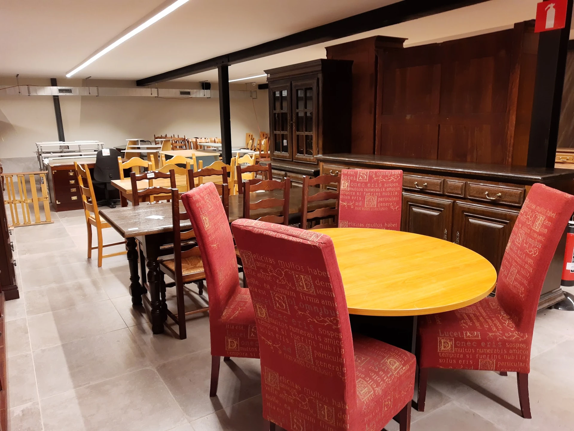 Winkelvloer met ronde gele tafel en rode stoelen, houten meubelstukken en kastjes op de achtergrond