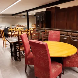 Winkelvloer met ronde gele tafel en rode stoelen, houten meubelstukken en kastjes op de achtergrond