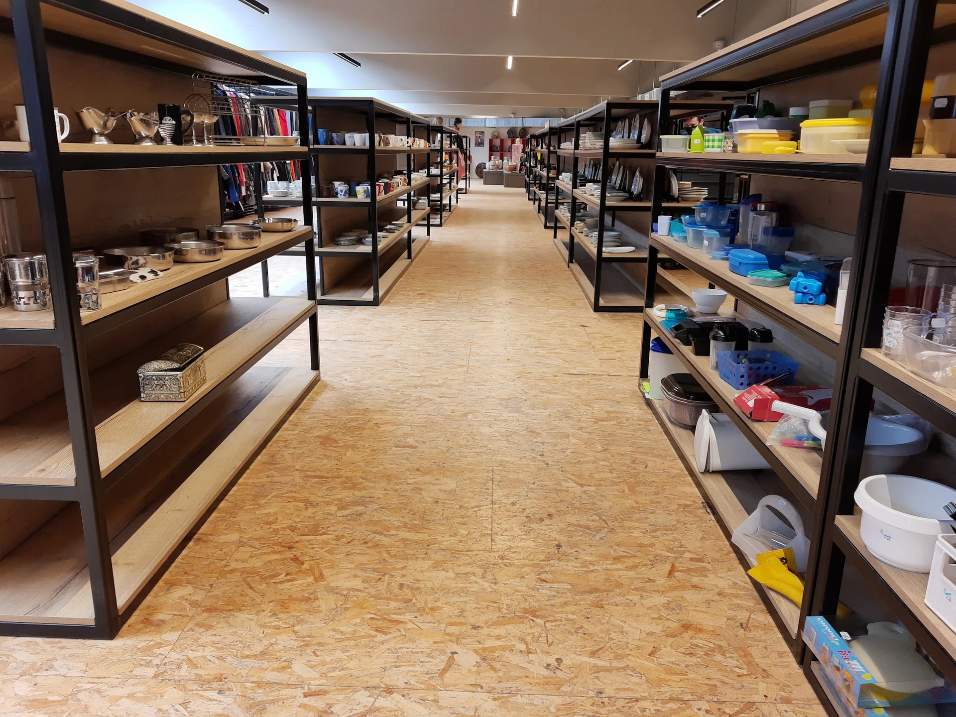 Winkelinterieur met donkere metalen stellingen langs beide zijden vol met boeken, decoraties en huishoudartikelen