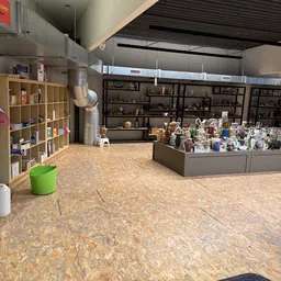 Winkelvloer met houten stellingen, vitrinekast met decoratieve artikelen en groen afvalbak