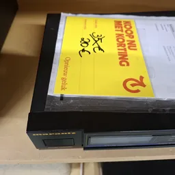 Gele waarschuwingssticker met rode tekst op een zwart apparaat
