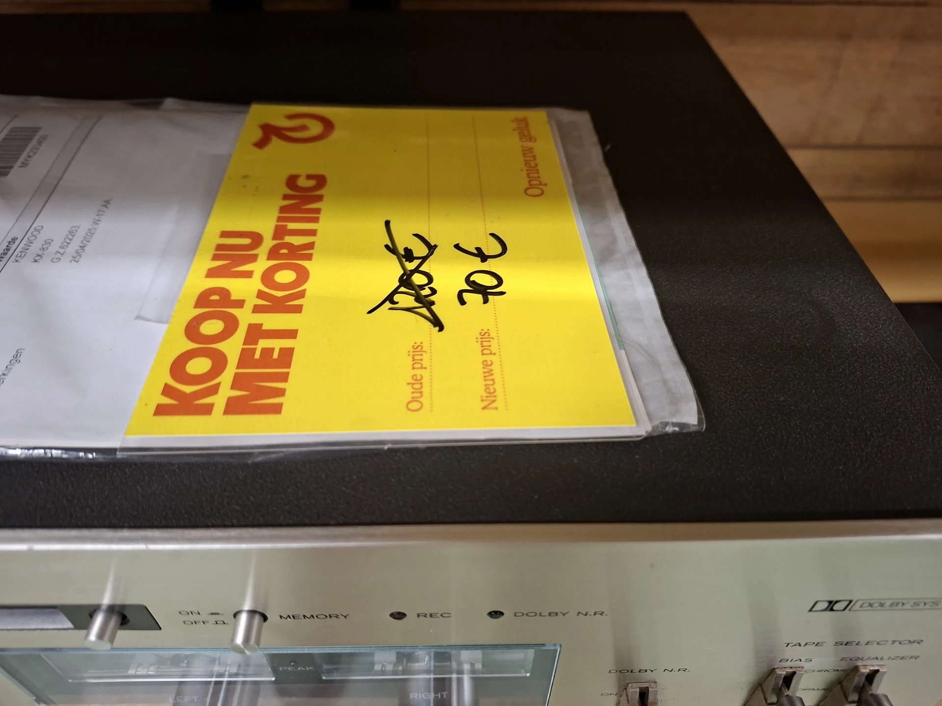Geel boek met rode tekst 'Koop bij Nettotting' op een plank, gedeeltelijk ingepakt in plastic