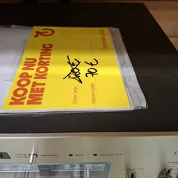 Geel boek met rode tekst 'Koop bij Nettotting' op een plank, gedeeltelijk ingepakt in plastic