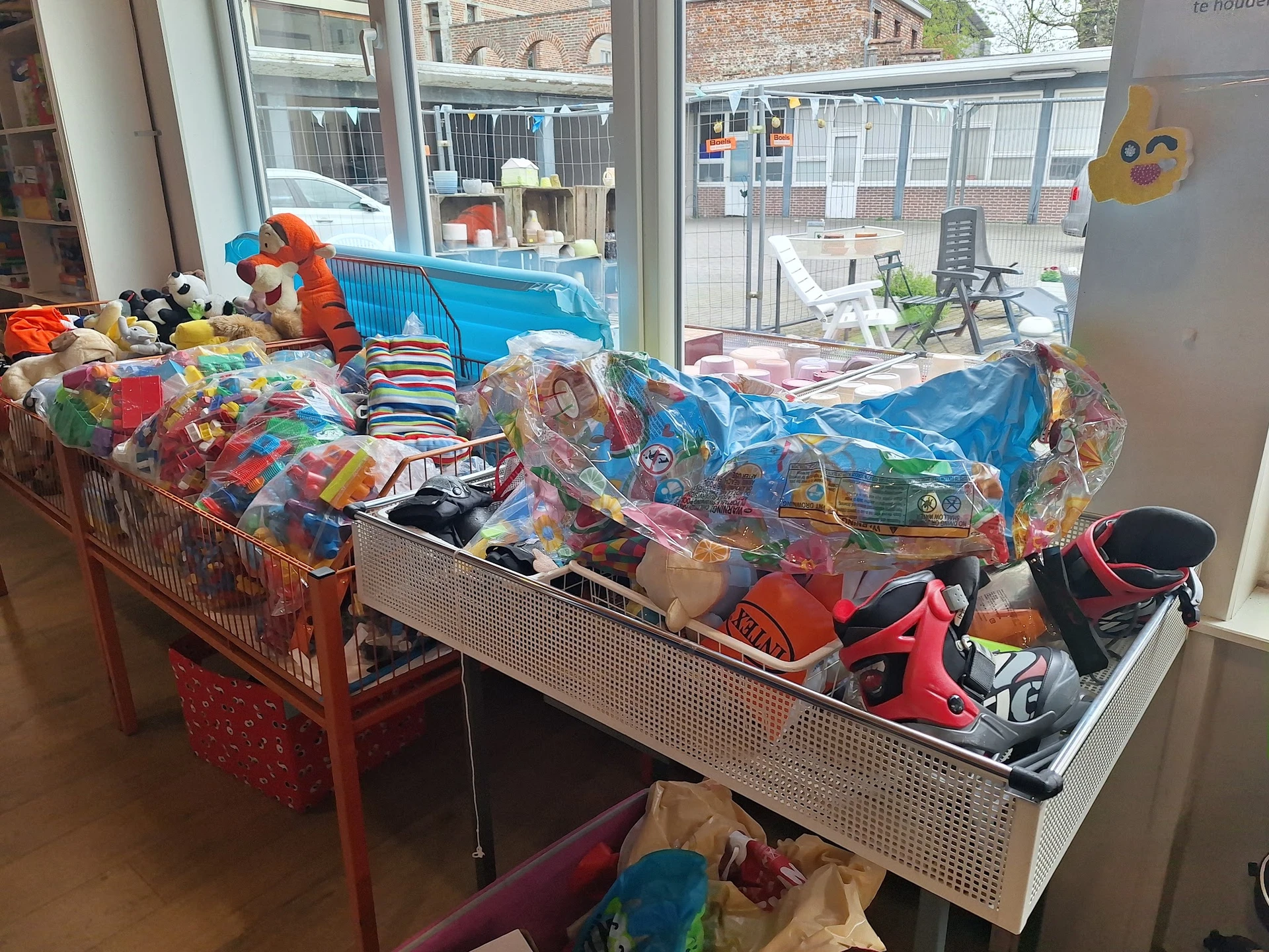 Tafels vol met kinderkleding en speelgoed in plastic verpakkingen in een kringloopwinkel