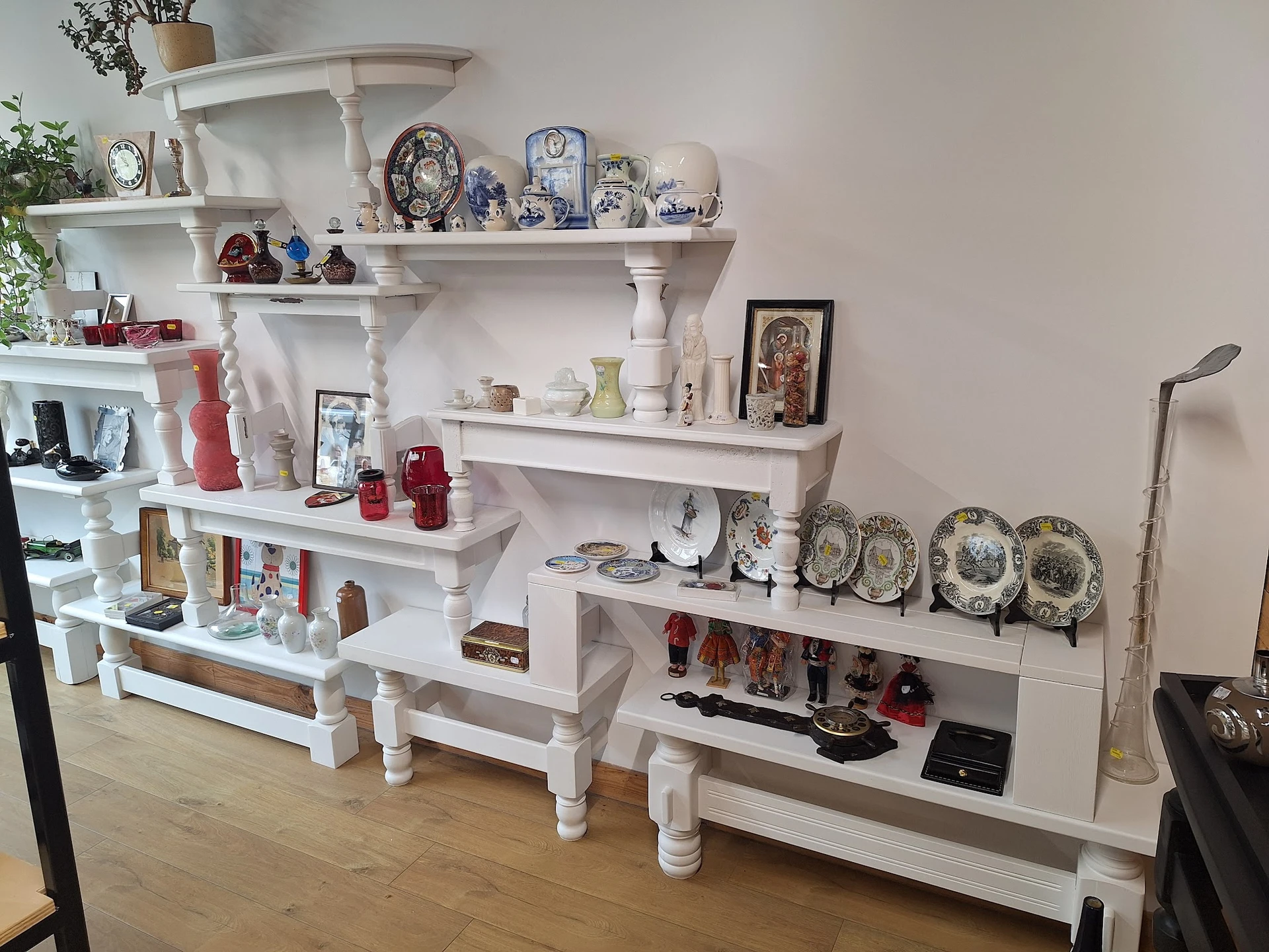 Witte wandplanken met decoratief serviesgoed, borden, kandelaars en huishoudartikelen uitgestald