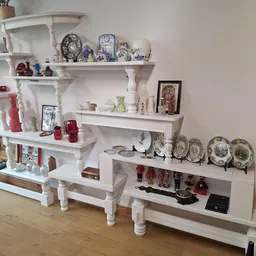 Witte wandplanken met decoratief serviesgoed, borden, kandelaars en huishoudartikelen uitgestald