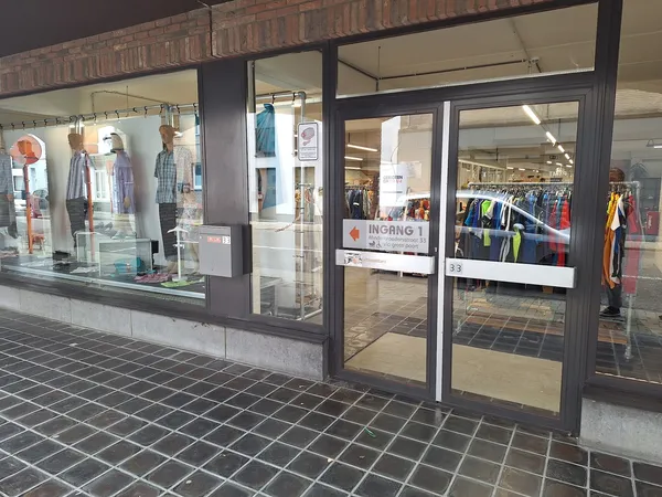 Winkelgevel met glazen deuren en ramen, kleding zichtbaar in etalage