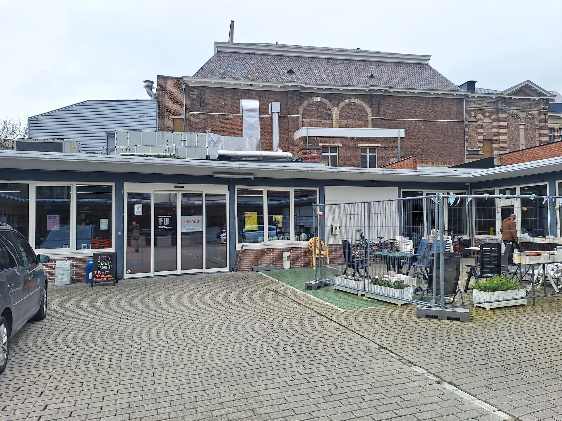 Voorgevel van kringloopwinkel met ingang, winkelramen en terras met stoelen