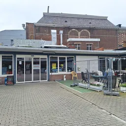 Voorgevel van kringloopwinkel met ingang, winkelramen en terras met stoelen