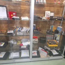 Glazen vitrinekast met diverse tweedehands elektronische apparaten, boeken, gamingartikel en andere items