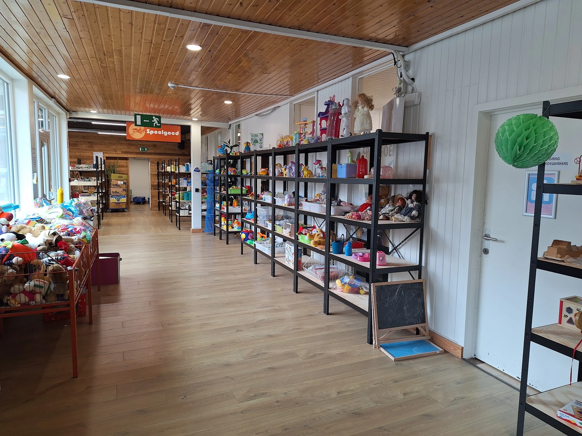 Winkelvloer van kringloopwinkel met zwarte stellingen vol spullen, houten plafond en diverse artikelen