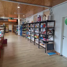 Winkelvloer van kringloopwinkel met zwarte stellingen vol spullen, houten plafond en diverse artikelen