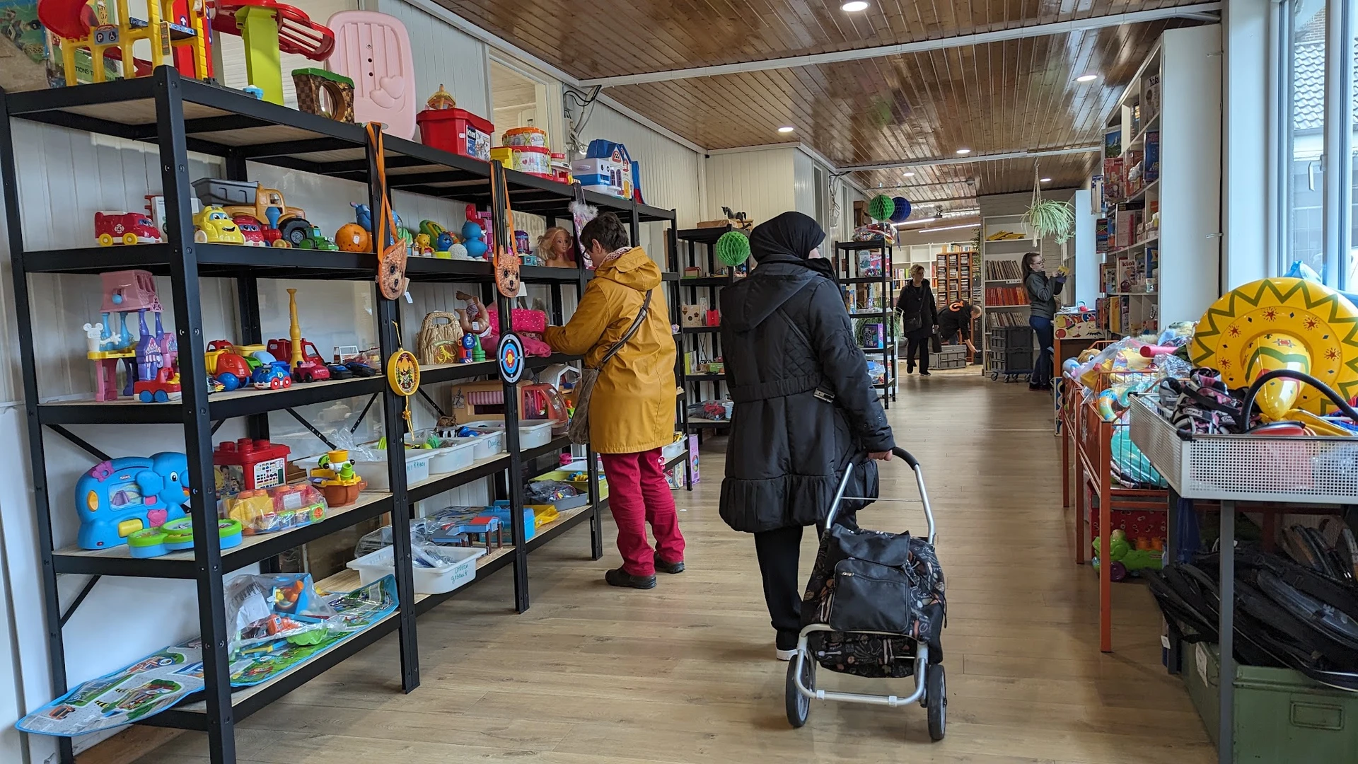 Winkelinterieur met speelgoed en boeken in stellingen, klanten winkelen, houten vloer