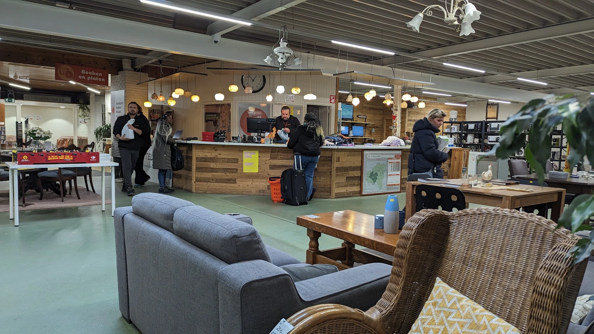 Winkelvloer met zitmeubels, tafels en baliebereik; klanten en personeel in de kringloopwinkel