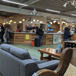 Winkelvloer met zitmeubels, tafels en baliebereik; klanten en personeel in de kringloopwinkel