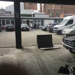 Parkeerplaats met auto's voor een winkel, gezien vanaf binnenuit achter glas