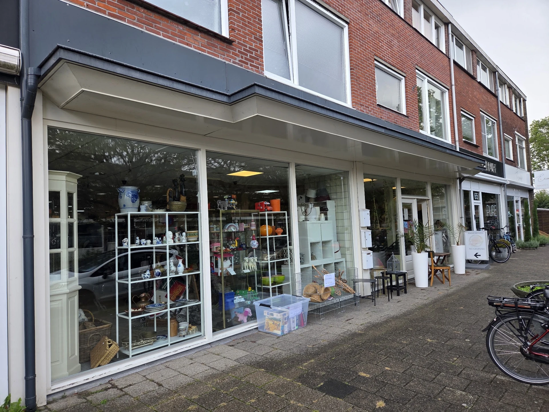 Winkelpui van kringloopwinkel met grote etalageruiten vol uitgestalde spullen, witte pui en rode bakstenen voorgevel
