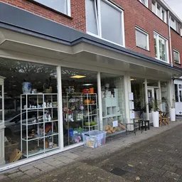Winkelpui van kringloopwinkel met grote etalageruiten vol uitgestalde spullen, witte pui en rode bakstenen voorgevel