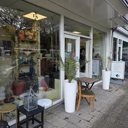 Winkelgevel met grote glazen ramen, witte deurkozijnen, plantenbakken en uitgestalde spullen op straat