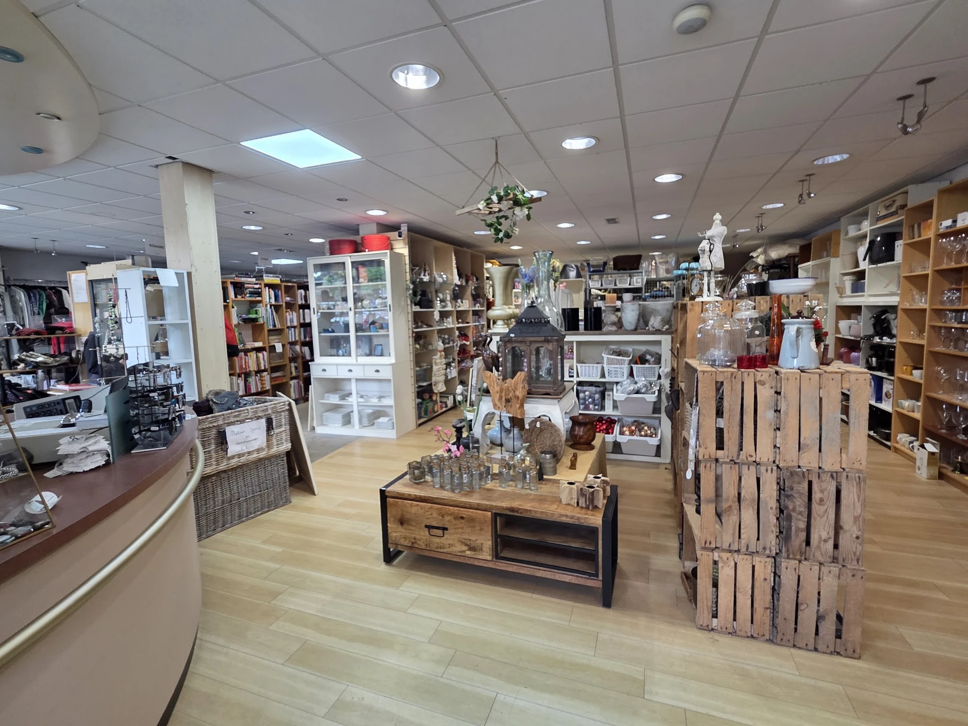 Overzicht van de winkelvloer met rekken, vitrines, houten toonbank en uitgestalde merchandise in een kringloopwinkel