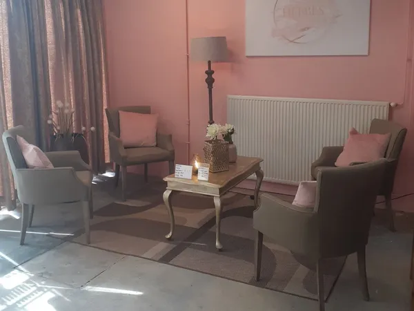 Ingerichte zithoek met roze wand, fauteuils, tafel en verwarming in kringloopwinkel