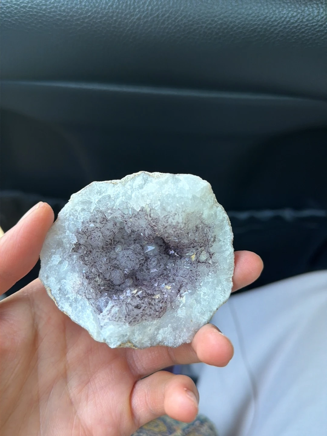 Close-up van een geode of kristalgeode met witte en paarse kristallen in een hand