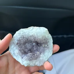 Close-up van een geode of kristalgeode met witte en paarse kristallen in een hand