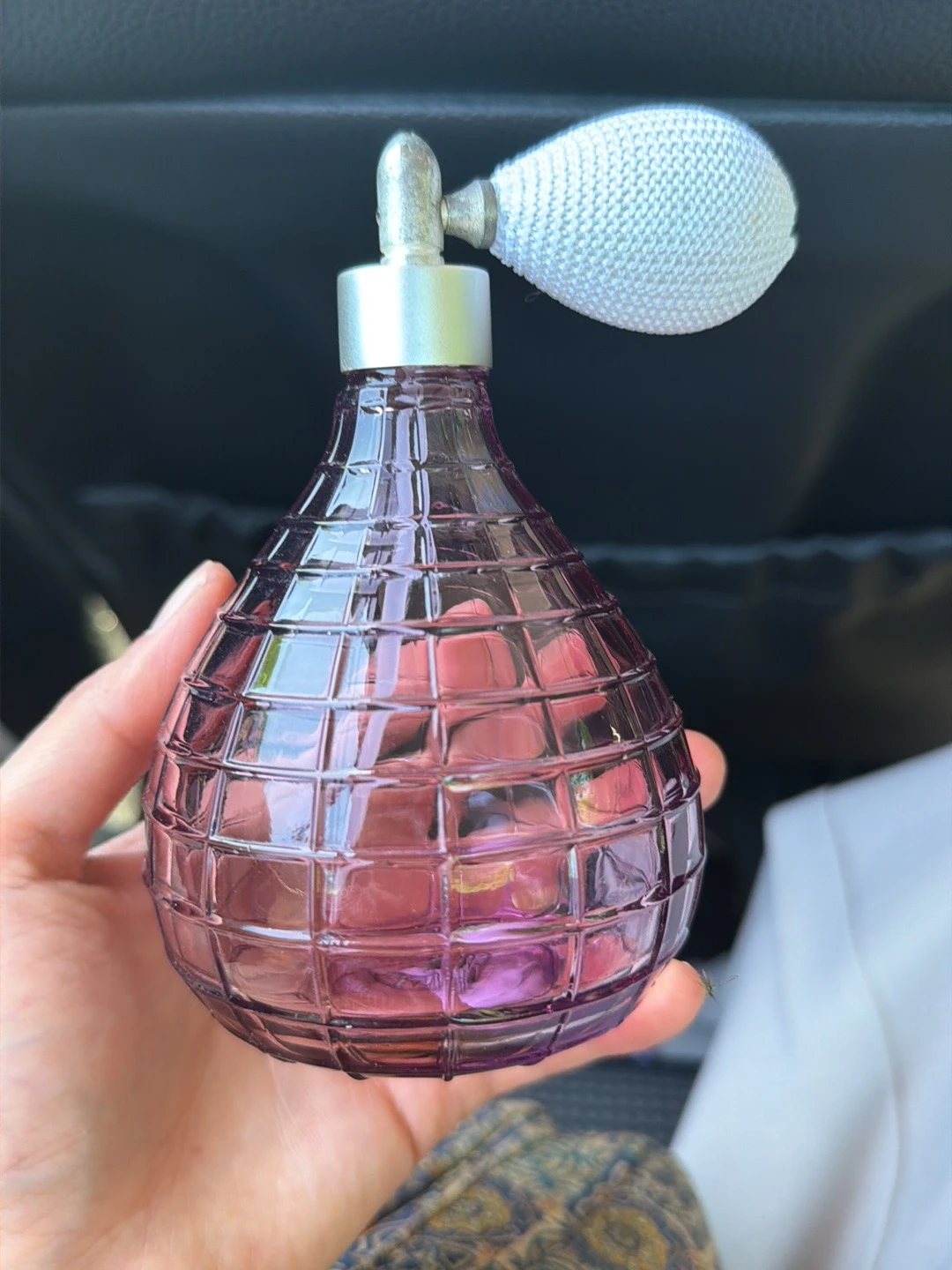 Close-up van een roze/paarse geurverstsproeier met ruitpatroon, gehouden in een hand