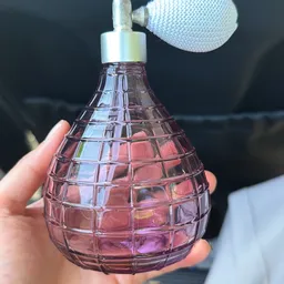Close-up van een roze/paarse geurverstsproeier met ruitpatroon, gehouden in een hand