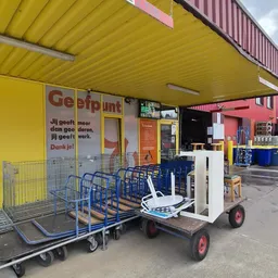 Gele gevel van kringloopwinkel met blauwe winkelwagens en rode deur, winkelname 'Geefpunt' zichtbaar