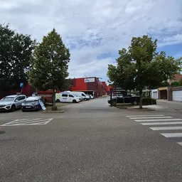 Parkeerplaats met enkele auto's en rode bedrijfspanden op achtergrond