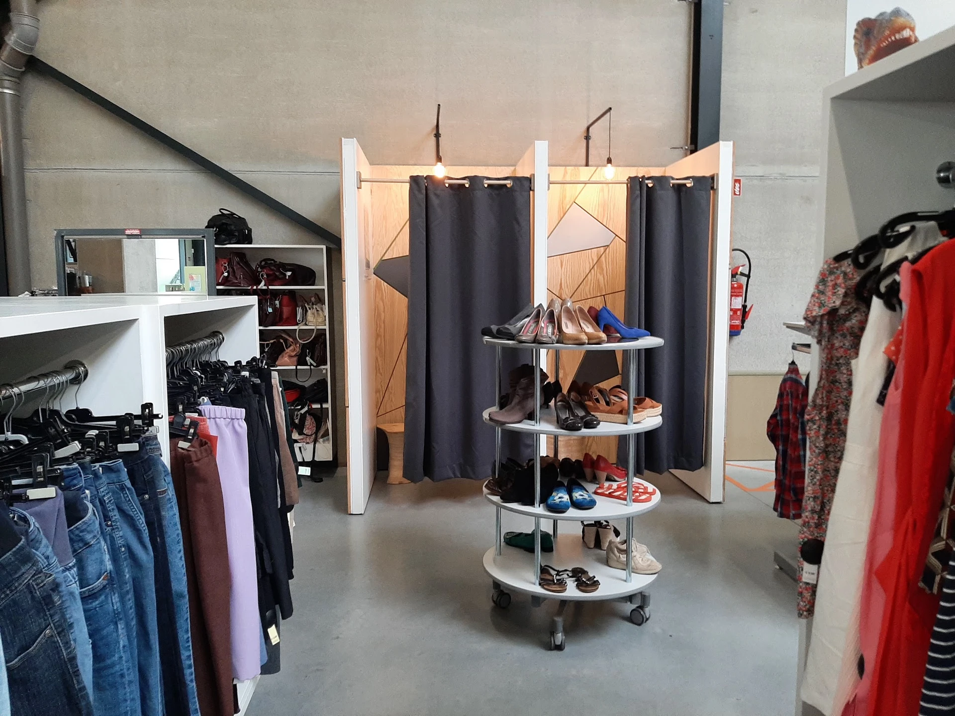 Winkelvloer met kledingrekken, een ronde displaytafel met schoenen en een paskamer met zwarte gordijnen