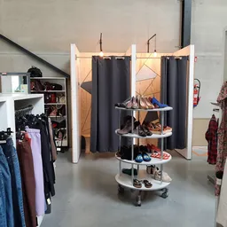 Winkelvloer met kledingrekken, een ronde displaytafel met schoenen en een paskamer met zwarte gordijnen