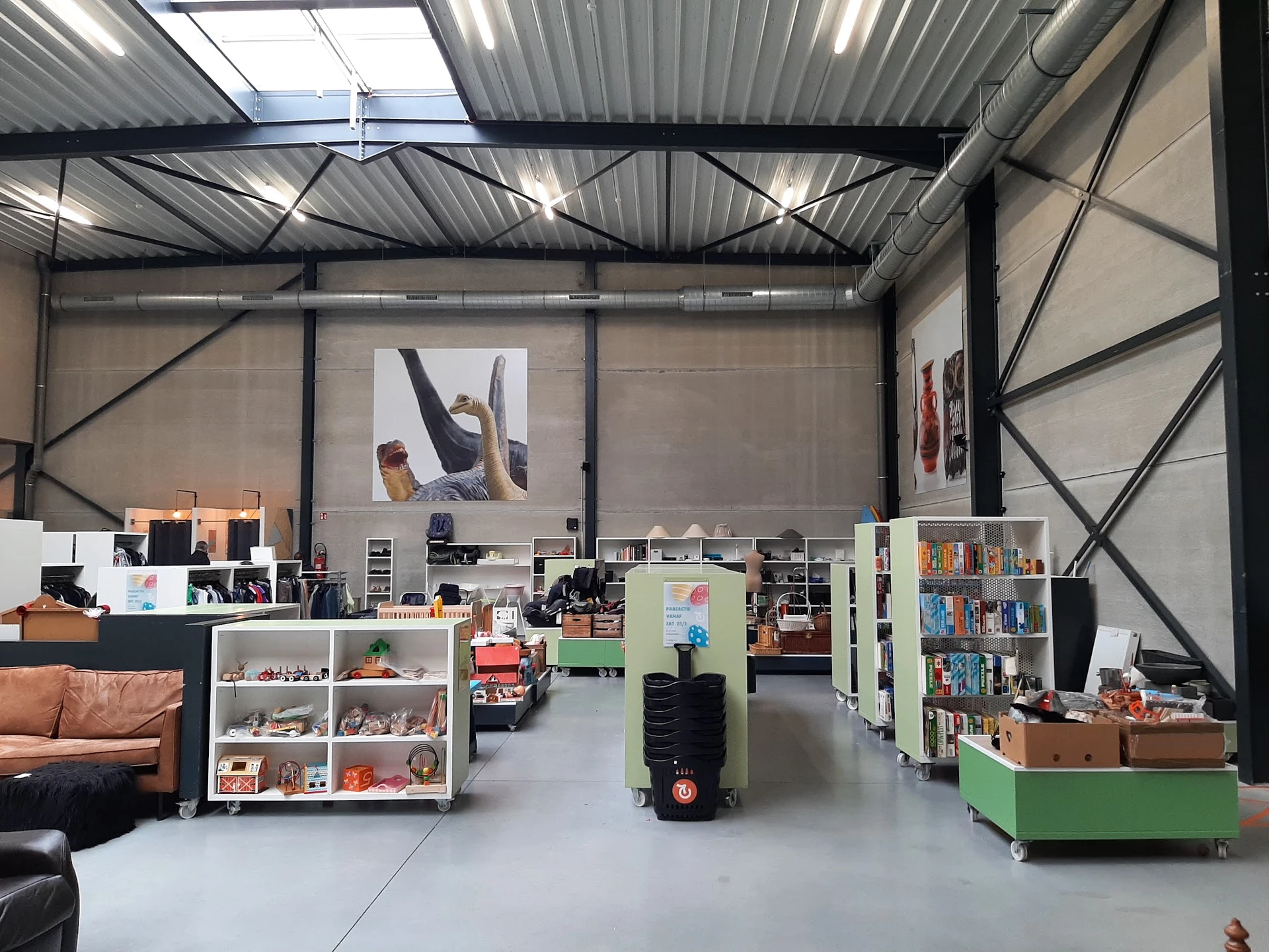 Winkelvloer van kringloopwinkel met boekenkasten, stellingen, groene verrijdbare bak en diverse tweedehands spullen