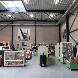 Winkelvloer van kringloopwinkel met boekenkasten, stellingen, groene verrijdbare bak en diverse tweedehands spullen