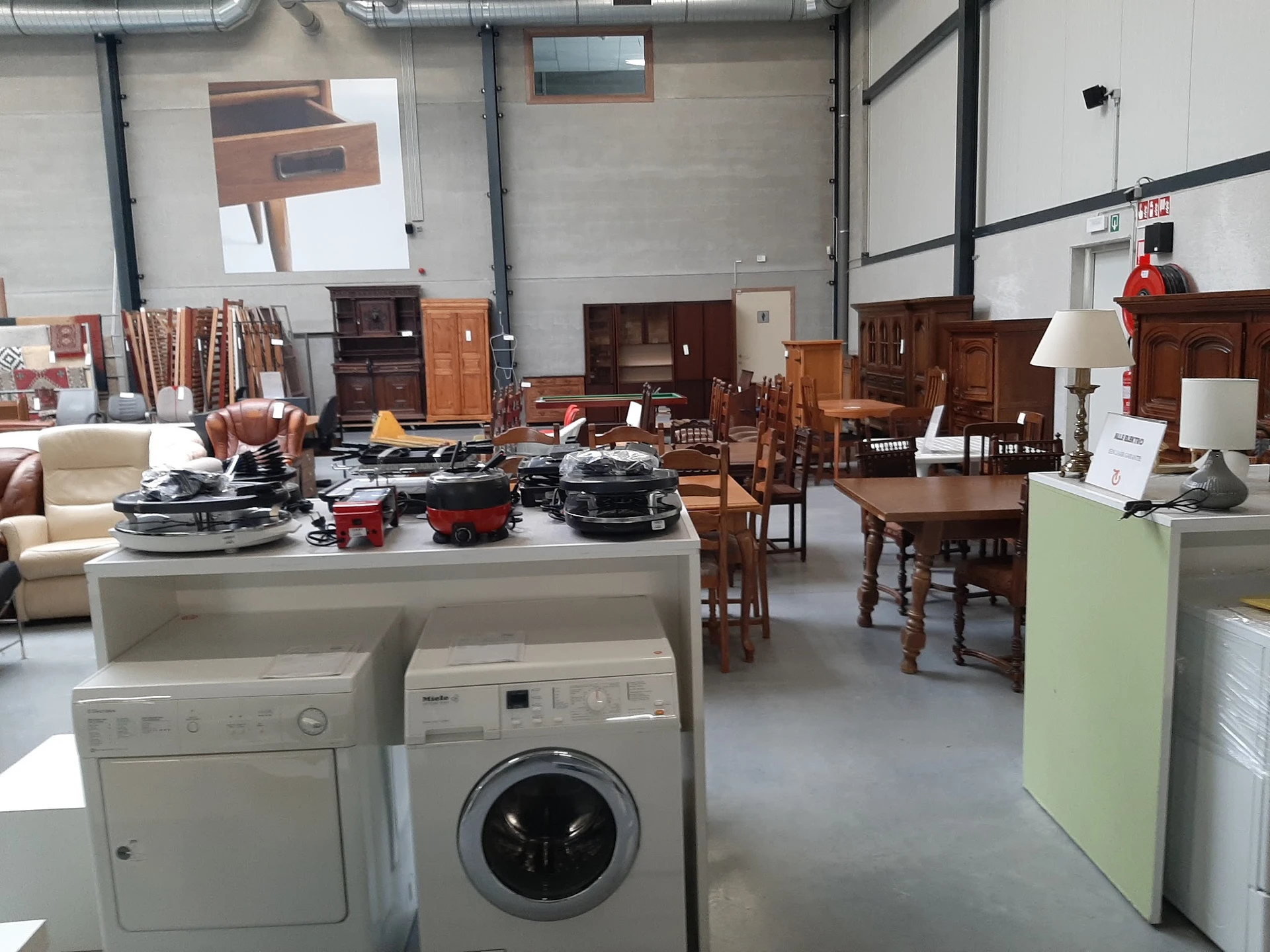 Kringloopwinkelinterieur met huishoudapparaten, meubilair en huisraad uitgestald op de vloer en tegen de muren