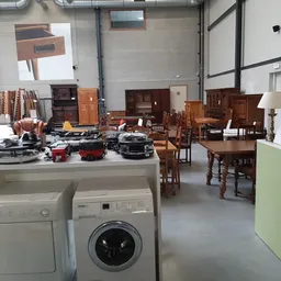 Kringloopwinkelinterieur met huishoudapparaten, meubilair en huisraad uitgestald op de vloer en tegen de muren