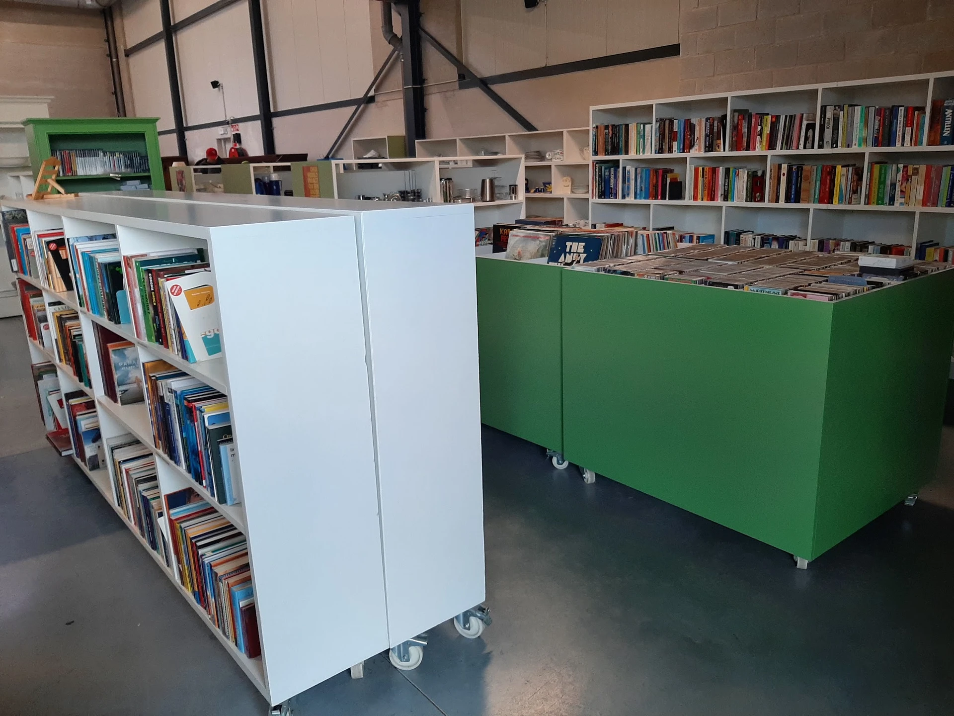 Binnenaanzicht van kringloopwinkel met witte en groene boekenkasten op wielen en boekenrekken op de achtergrond