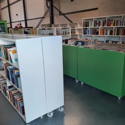 Binnenaanzicht van kringloopwinkel met witte en groene boekenkasten op wielen en boekenrekken op de achtergrond