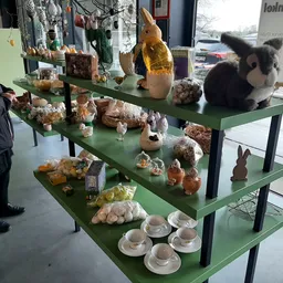 Groene display-tafels met diverse gebruiksartikelen en decoratieve items zoals servies, houten beeldjes en potten