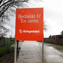 Rood welkomstbord met 'Bedankt & Tot ziens' en Kringwinkel-logo bij de ingang van de winkel