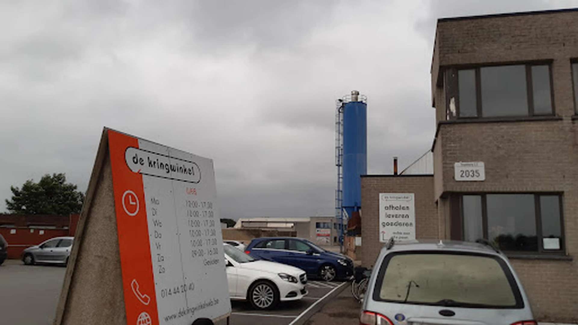 Parkeerterrein met auto's en bedrijfsgebouwen onder bewolkte lucht