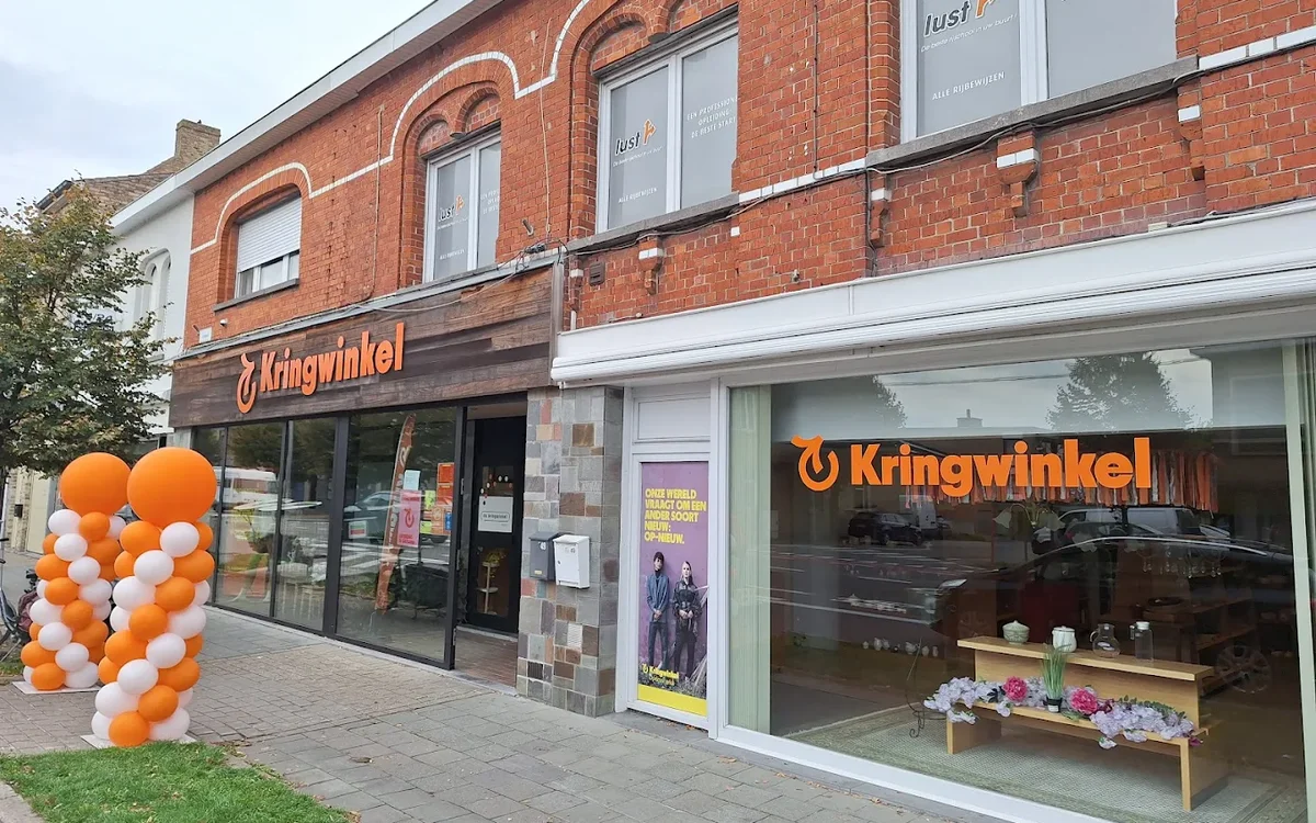Gevel van kringloopwinkel met oranje en witte ballonnen en grote ramen met etalage