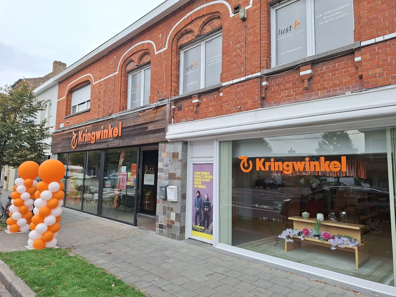 Gevel van kringloopwinkel met oranje en witte ballonnen en grote ramen met etalage