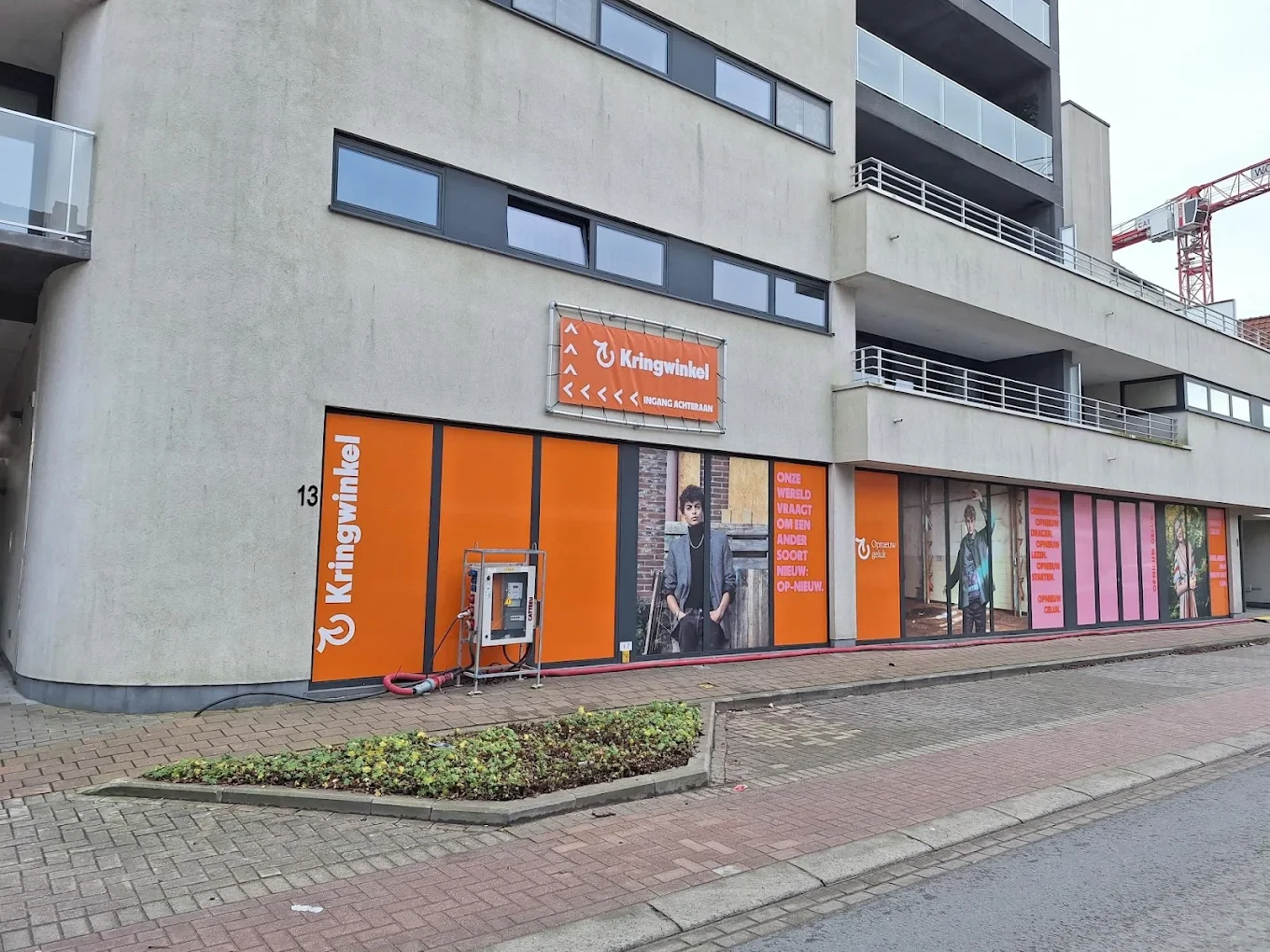 Gevel van kringloopwinkel met oranje en roze gevelbekleding, grote ramen en winkelname zichtbaar