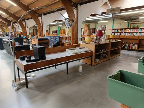 Ruim winkelbinnenruimte met houten balken, boekenrekken, meubels en verschillende afdeling van een kringloopwinkel