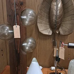 Close-up van drie zilvergrijze metalen bollampen met prijskaartjes, tegen houten wand